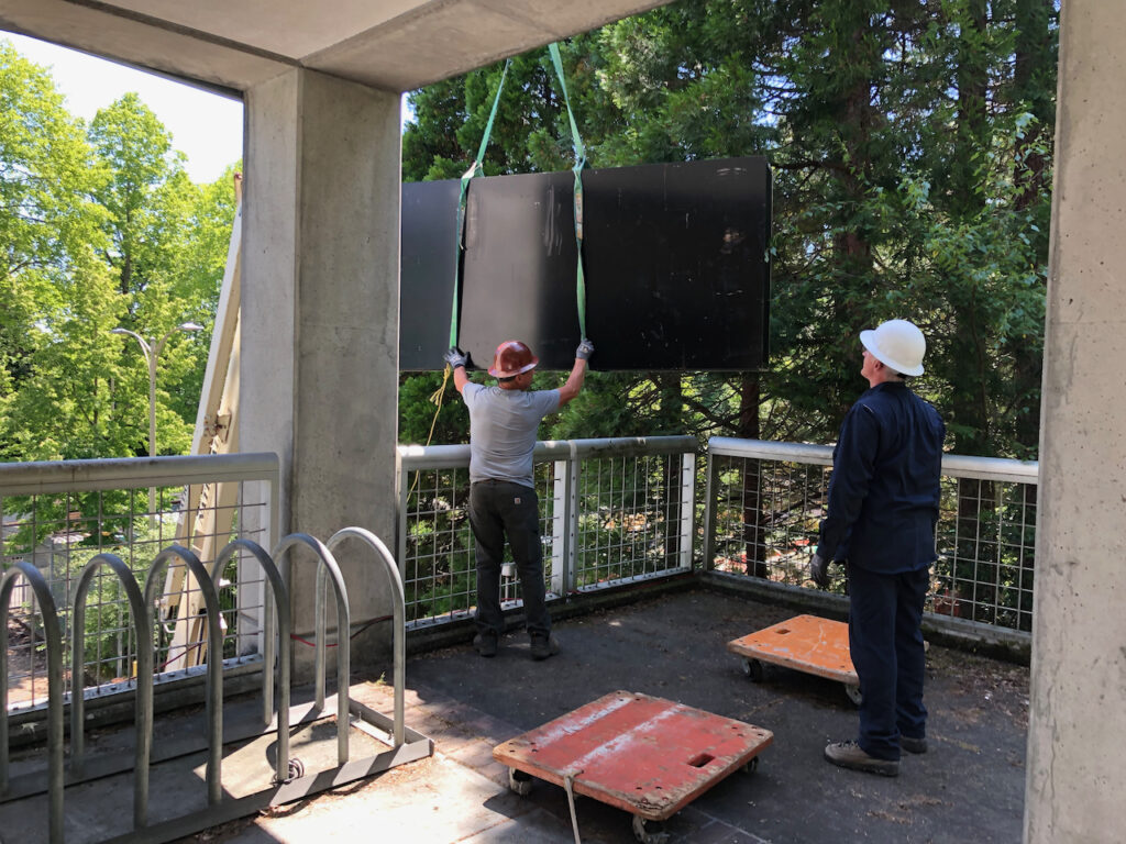 Workers move a giant black table to an upper story using a crane. 