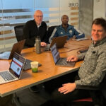 The team gathered around a table with Marion the video call. L-R Kevin, Scott, Gerard, Delwin, Lewis, David, and Vijay